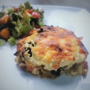 a portion of moussaka with salad in the background
