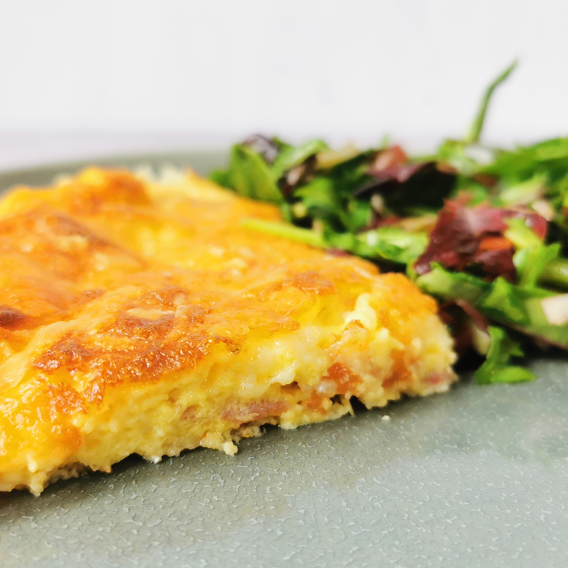 a triangle of quiche lorraine with a colourful sald on a grey plate