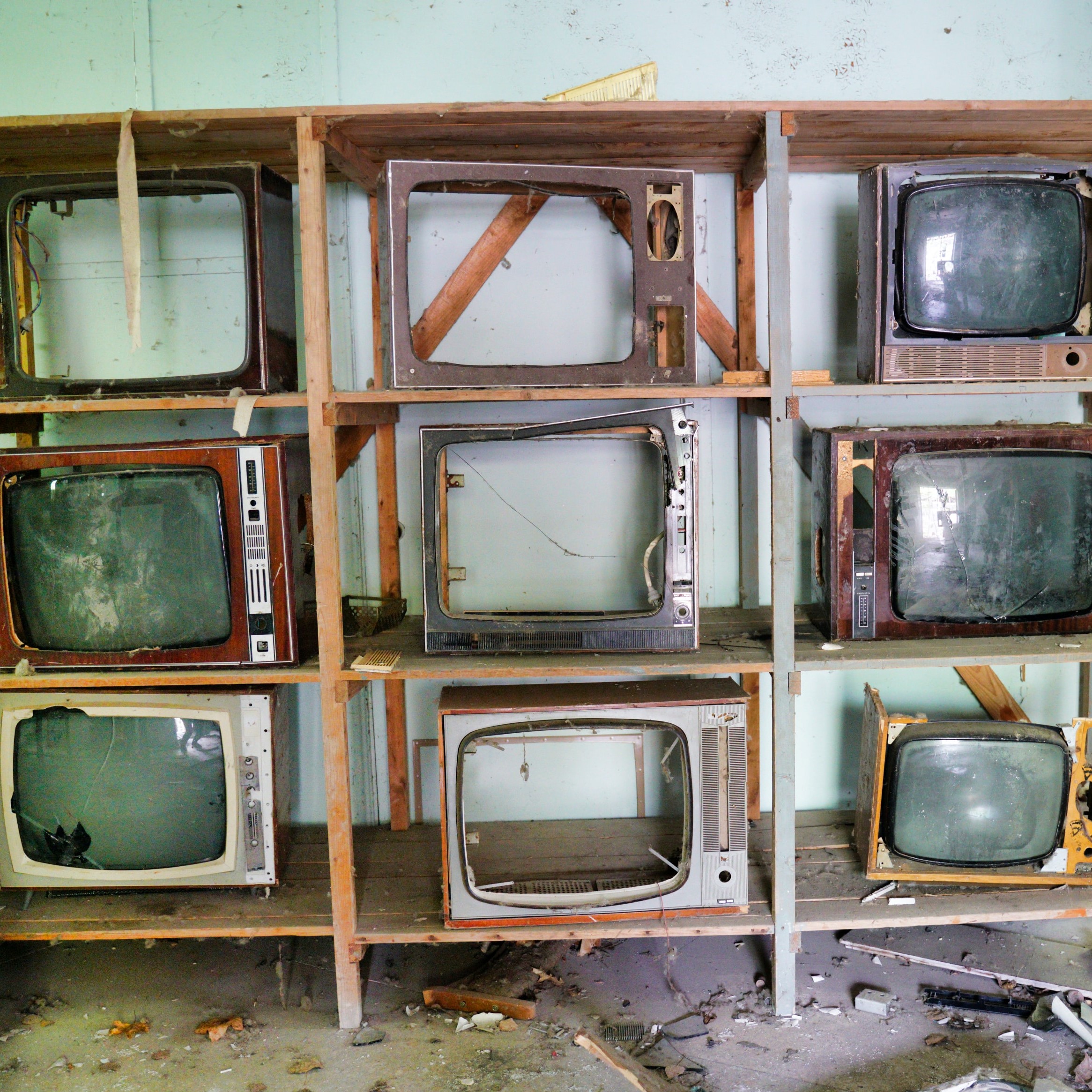 old tvs on a shelving unit with their screens smashed out