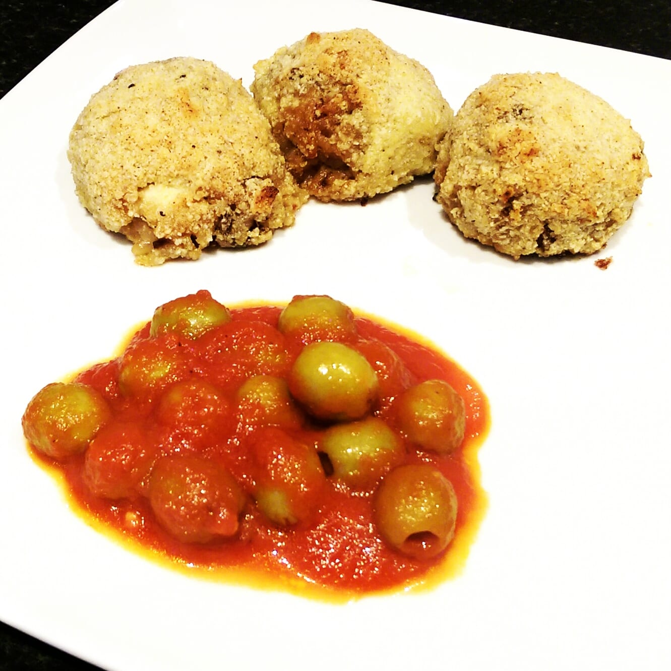 Three arancini balls with olive and tomato sauce