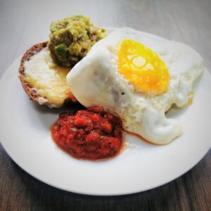 Golden yolked fried egg on a low carb roll with salsa and guacamole on a white plate placed on a wooden surface