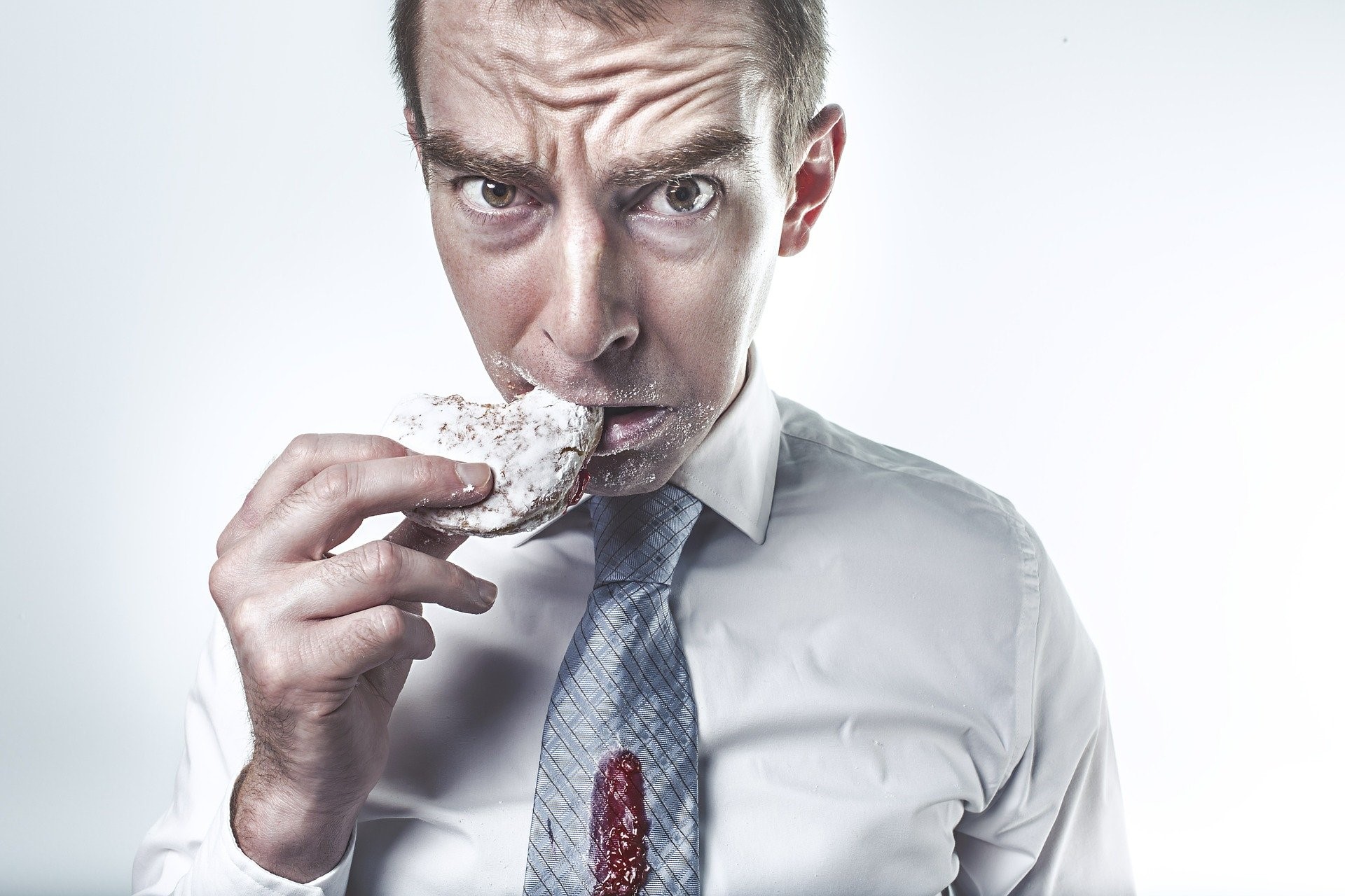 worried man eating a donut with jam spilled on his tie