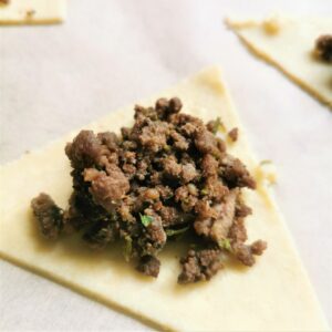 a triangle of uncooked low carb pastry and a spoonful of lamb samosa filling on top