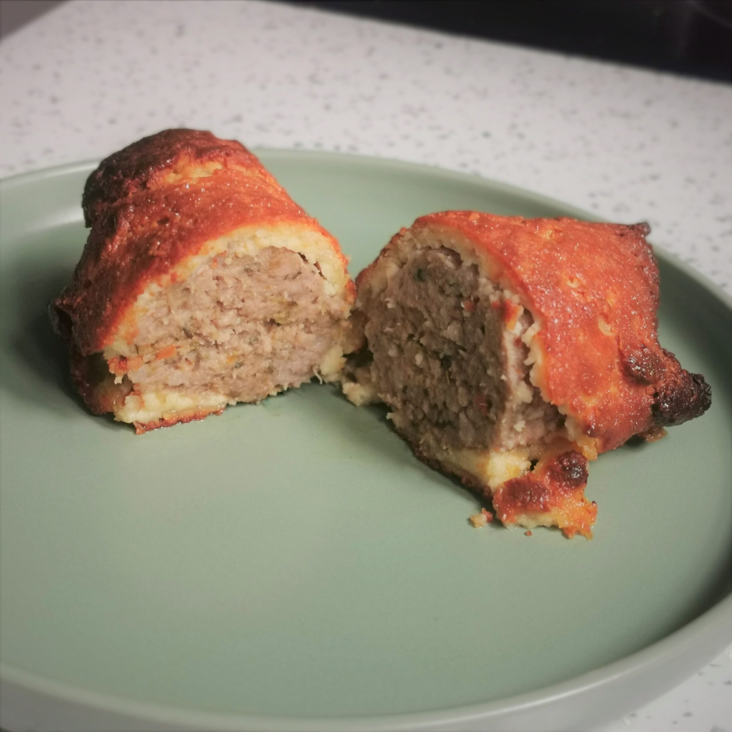 a low carb sausage roll cut in half on a green plate with a white kitchen surface