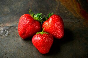 three strawberries on a grey surface