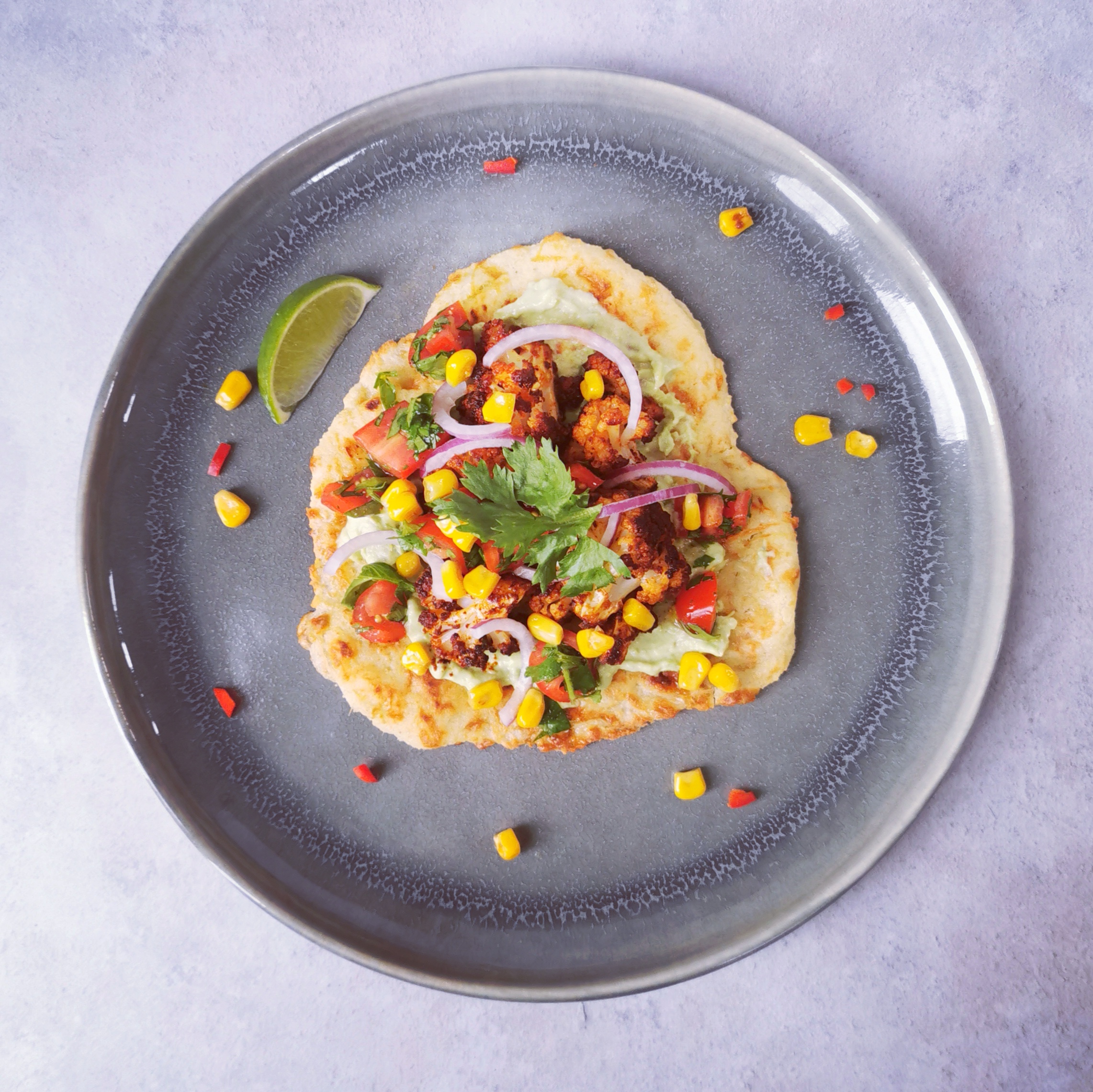 overhead view of a grey plate with a low carb taco. Topped with cauliflower, avocado cream, sweetcorn and coriander
