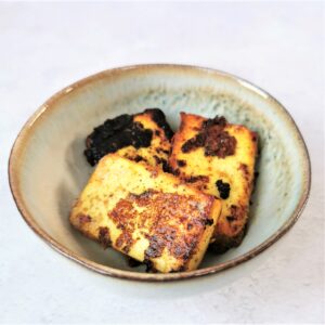 three rectangles of charred and marinated paneer cheese in a small brown rimmed bowl on a mottled background