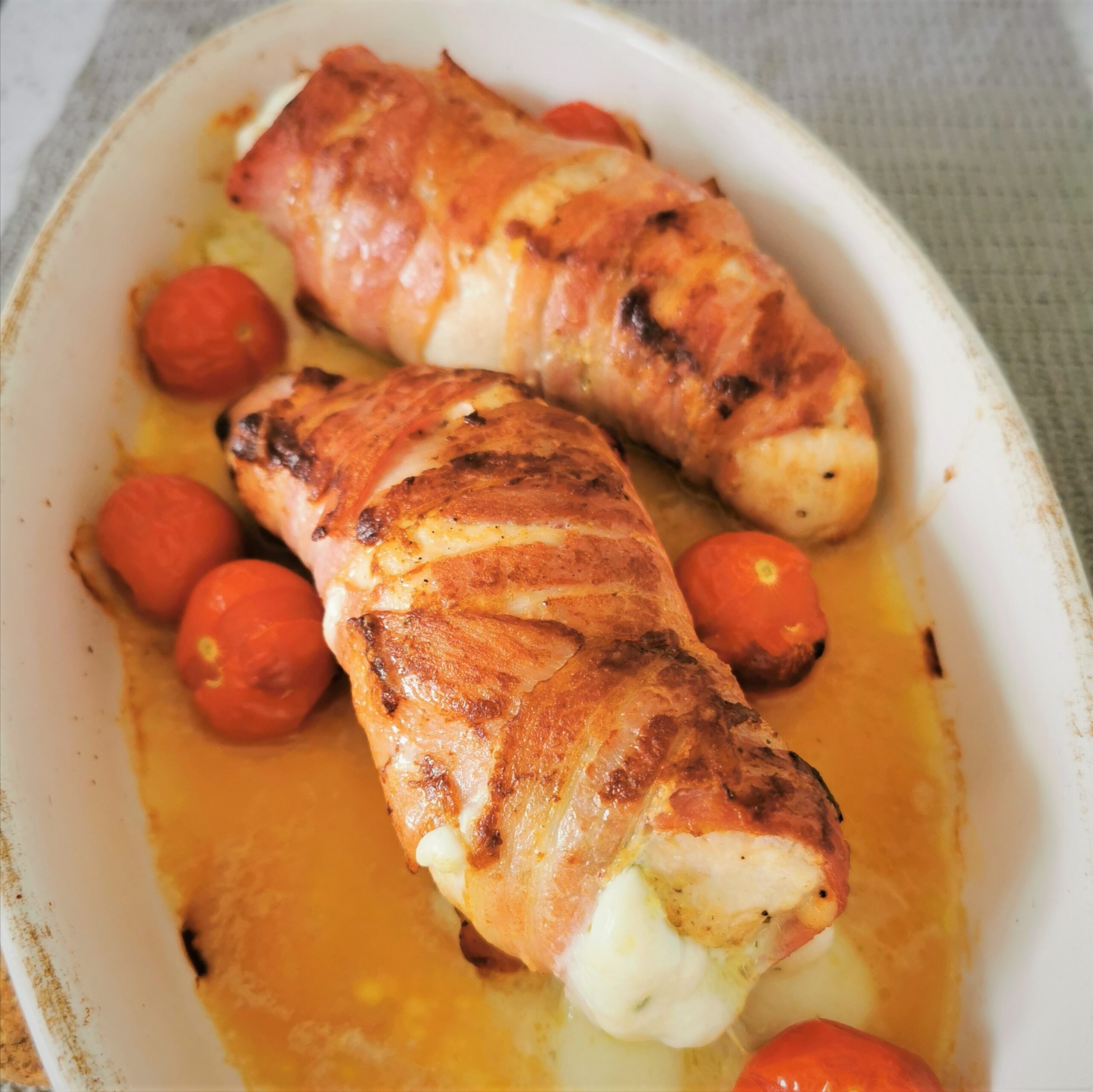 chicken breasts wrapped in bacon in a ceramic dish surrounded by baby tomatoes
