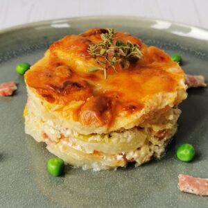close up of the layers of celeriac leek and bacon with peas and bacon bits on a grey plate