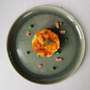 celeriac leek and bacon gratin on a grey plate with scattered peas and bacon pieces