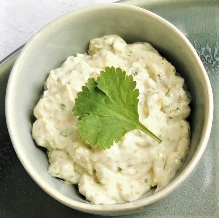 a small ceramic bowl containing lime and coriander tartare sauce with a fresh coriander leave on top