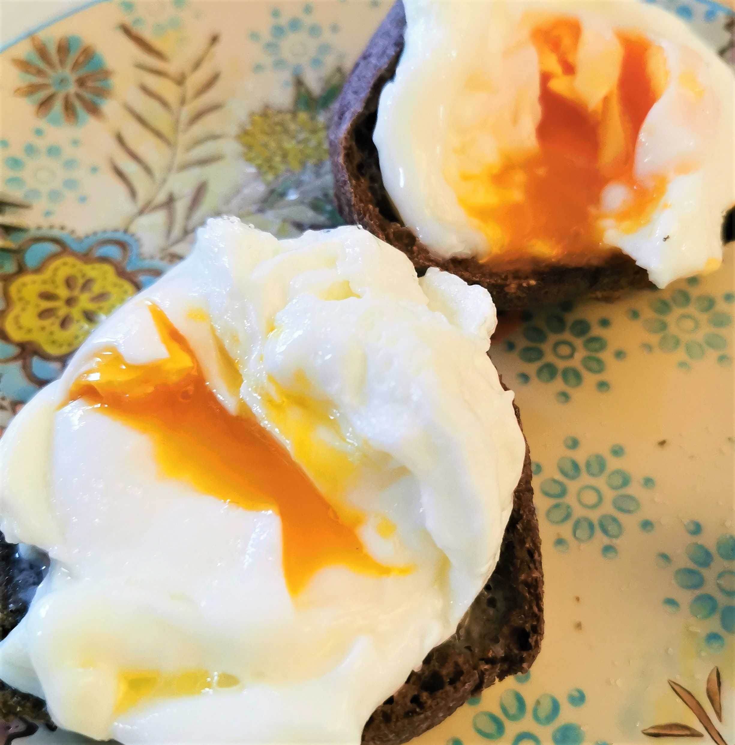 two poached eggs oozing golden yolk on two halves of low carb roll served on a patterned plate