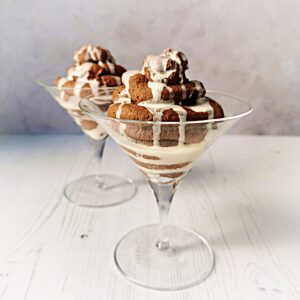 Two cocktail glasses filled with a spiral of chocolate mousse topped with double cream on a grey background