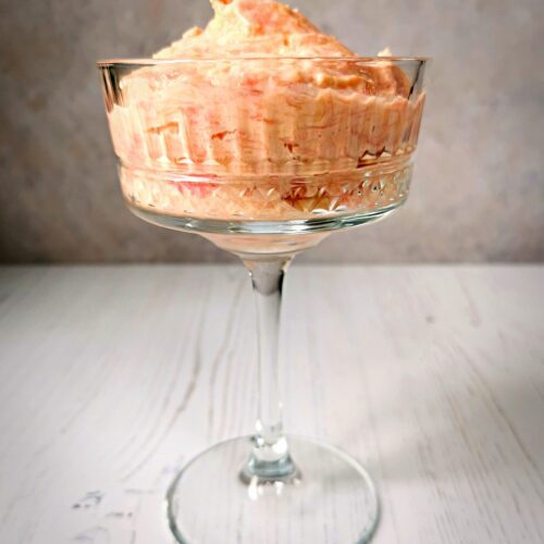 A tall stemmed glass filled with rhubarb fool on a grey background